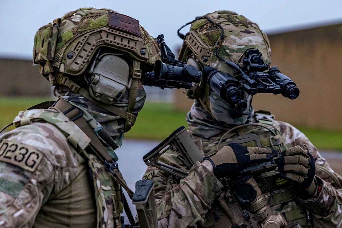 Two soldiers dressed in camouflage, observing with binoculars in a tactical setting.