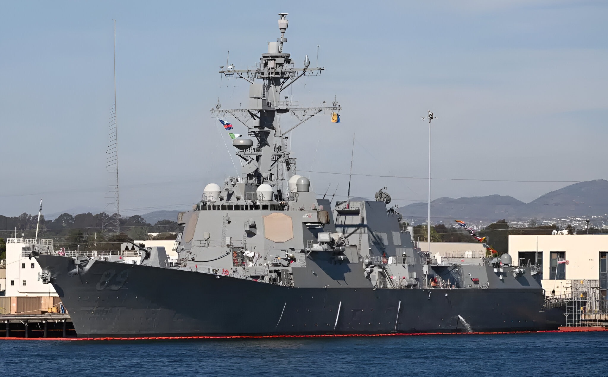 A modern U.S. Navy destroyer moored at port, showing its superstructure, sensors, and deck-mounted Mk 38 weapon system used for close-in surface defense.