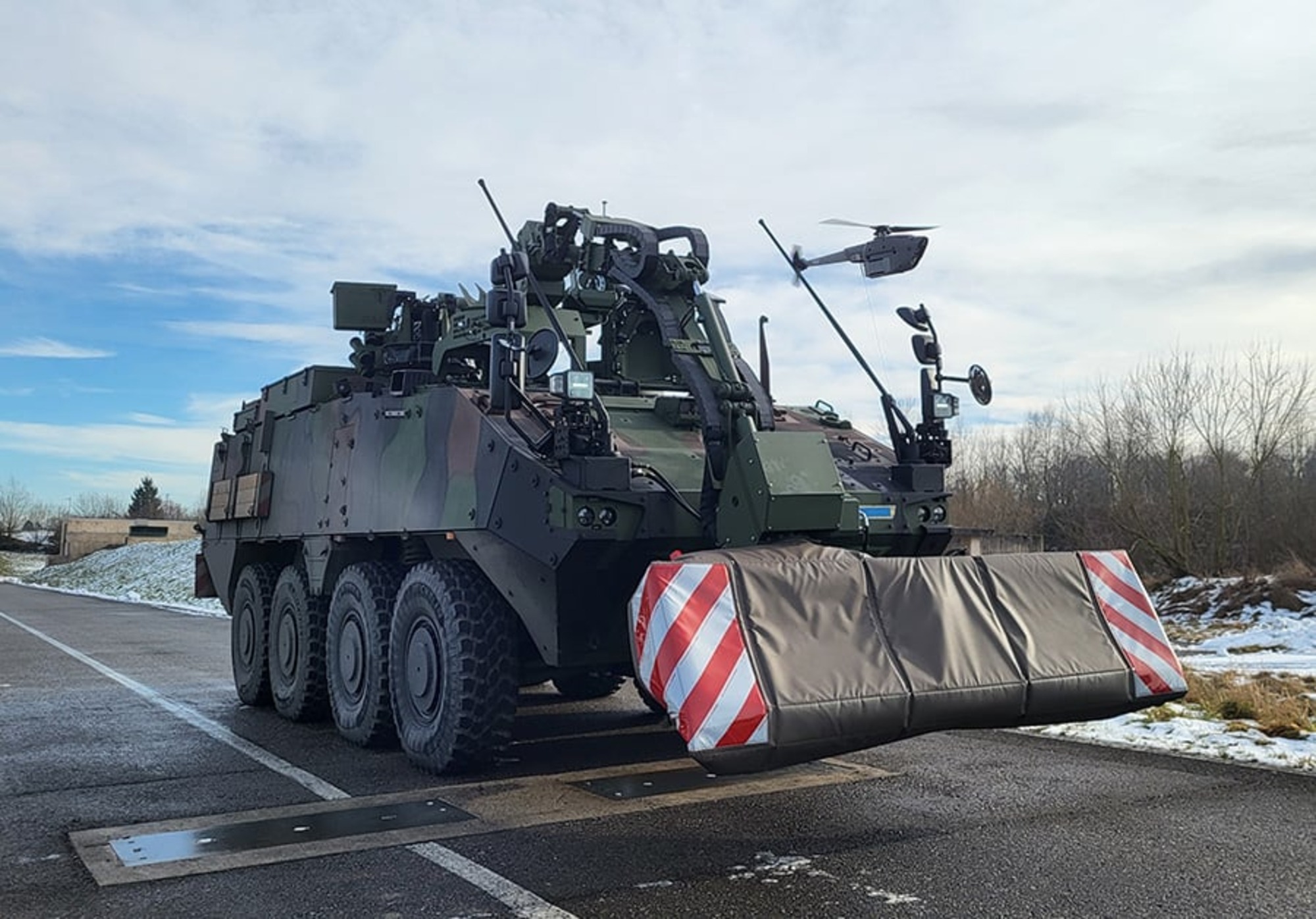 A Black Hornet nano drone hovering in front of a Piranha armored engineering vehicle