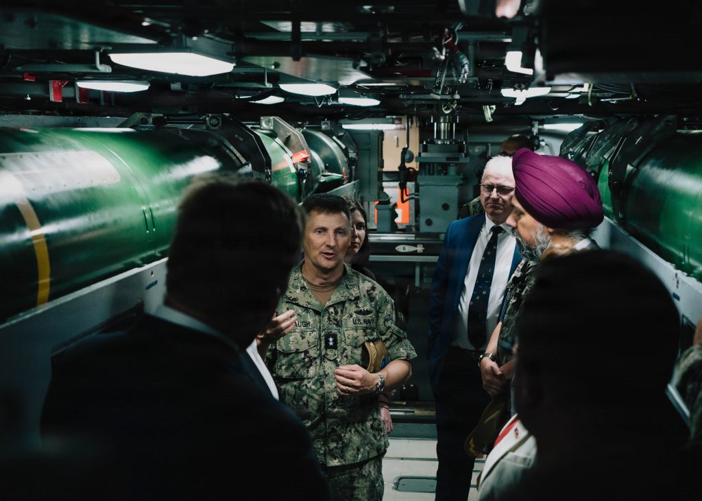 Rear Adm. Chris Cavanaugh, Commander, Submarine Force, U.S. Pacific Fleet, center, speaks with members of the U.K. House of Commons Defense Committee in the torpedo room aboard Virginia-class fast-attack submarine USS Vermont (SSN 792)