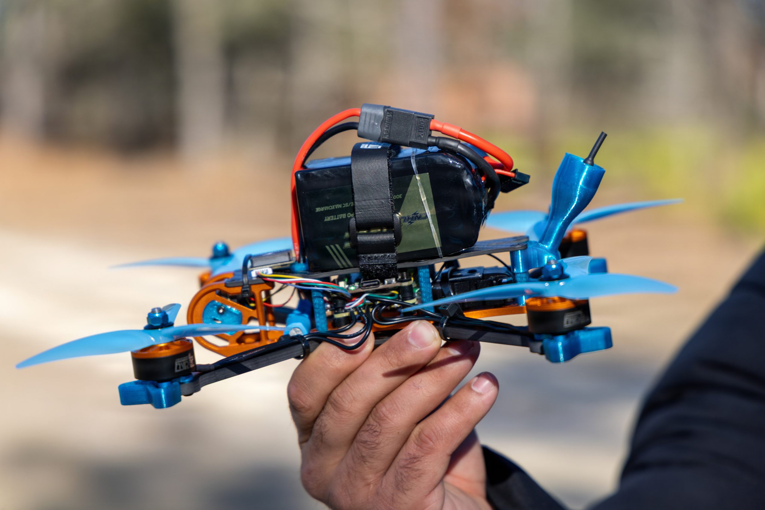 A U.S. Army Soldier assigned to 7th Special Forces Group (Airborne) holds a student-built FPV drone—complete with carbon fiber frame, blue propellers, orange anodized motors, strapped lithium-polymer battery, and exposed wiring—following successful assembly during the Operator Drone Basic Course at Eglin Air Force Base, Florida, Jan. 26, 2027. After Week 1 hands-on construction, troubleshooting, and simulator training, students walk away with a fully functional drone they built themselves, enabling Green Berets to deploy these unmanned systems for reconnaissance, precision observation, or action—placing robots in harm's way to protect personnel and enhance situational awareness on future battlefields. (U.S. Army photo by Sgt. Jacob Bradford)