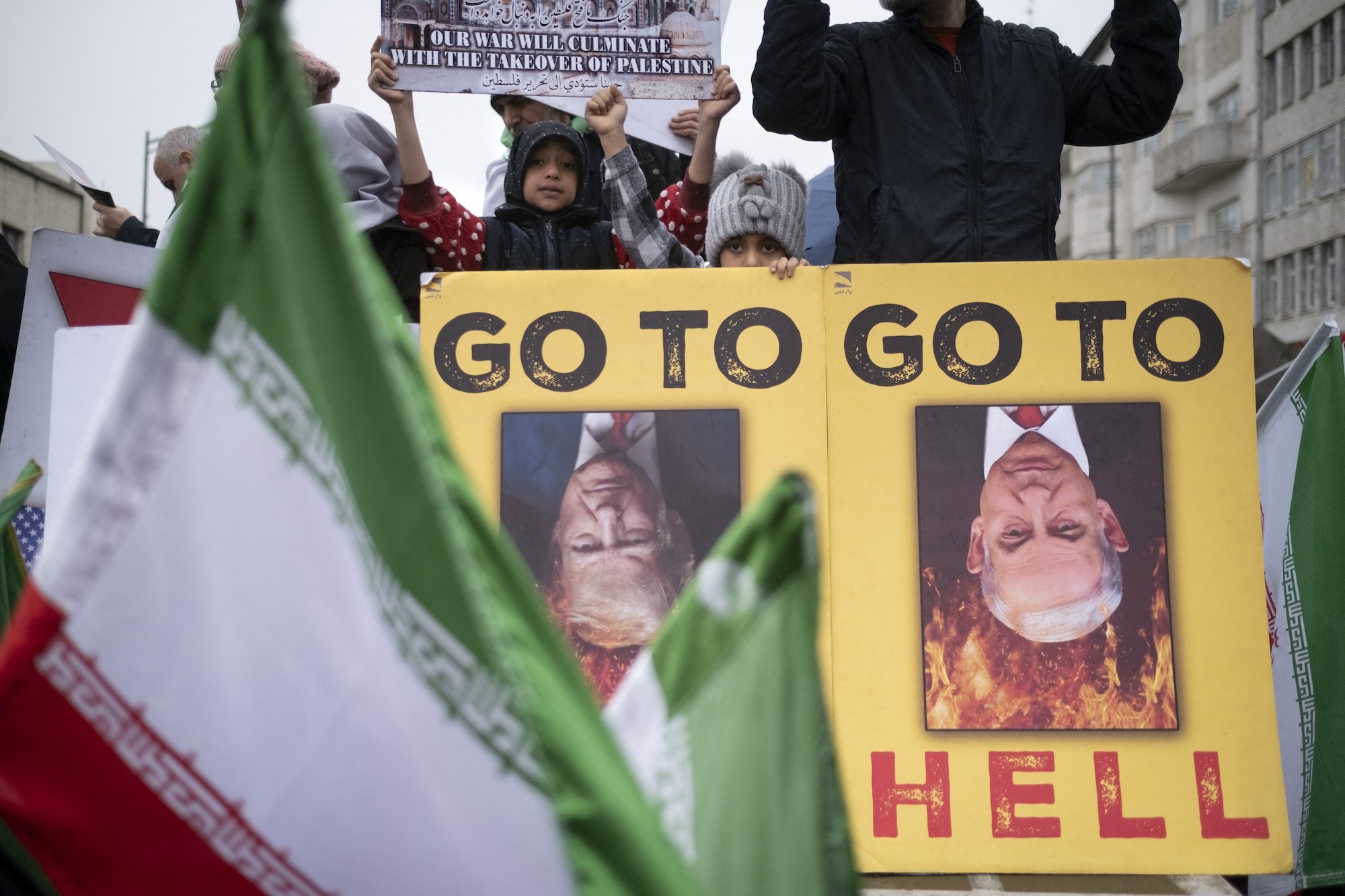 Iranian children stand behind an anti-US and anti-Israeli banner depicting portraits of US President Donald Trump and Israeli Prime Minister Benjamin Netanyahu in Tehran, Iran