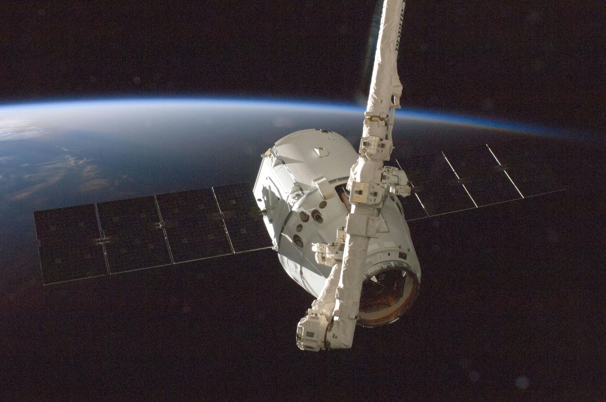 A SpaceX Dragon spacecraft orbits Earth with its solar arrays deployed.
