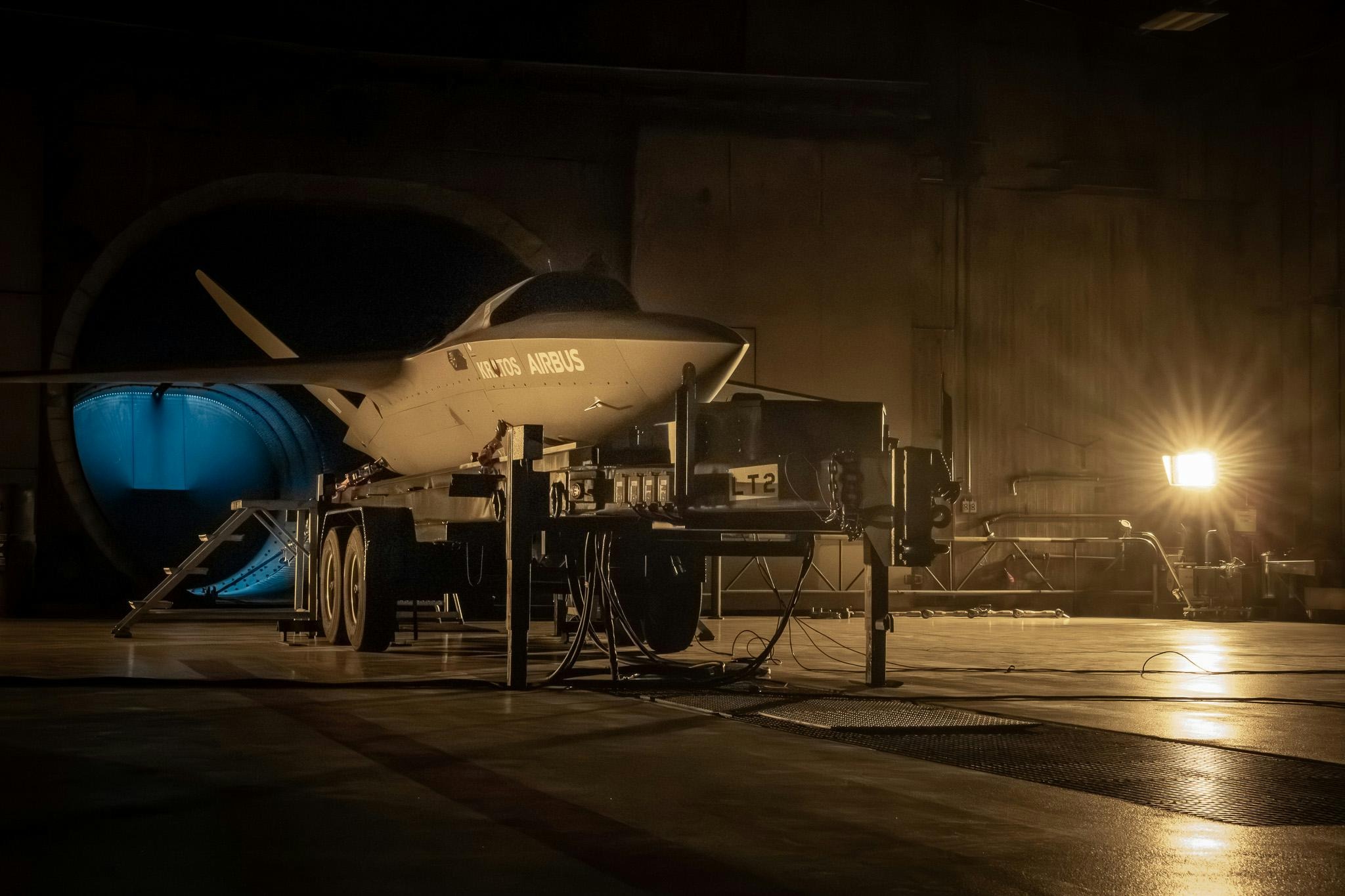 Kratos XQ-58 Valkyrie stealth drone displayed on a wheeled trailer inside a military hangar during low-light pre-flight or testing operations, co-branded with Airbus