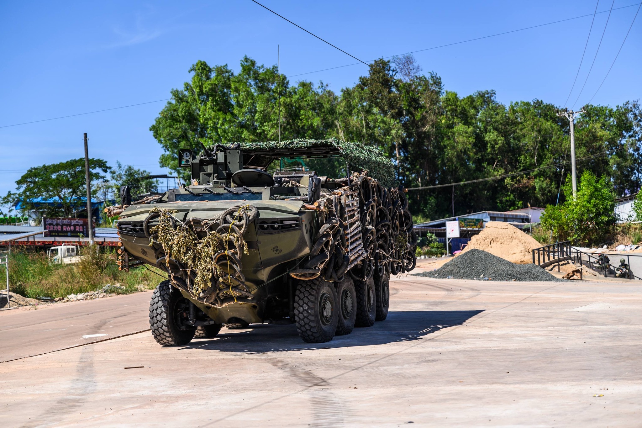 Royal Thai Navy amphibious 8x8 armored vehicle draped in camouflage netting and tire armor moving along a road during border defense operations