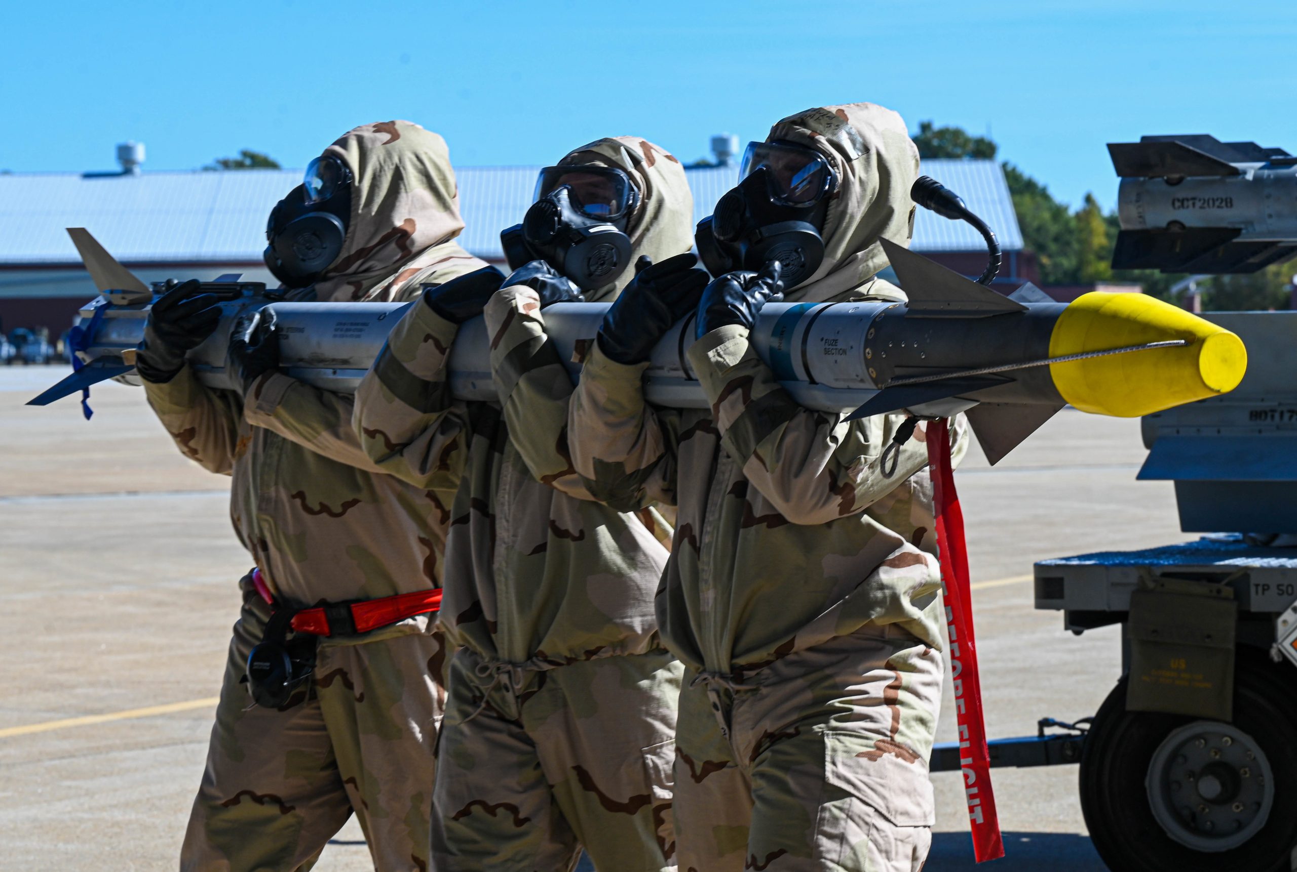 U.S. Air Force Staff Sgt. Jordan Spotswood, right, Tech Sgt. Zachary Warners, middle, and Tech. Sgt. Ambrose Kun, all 192d Aircraft Maintenance Squadron aircraft armament systems craftsmen, carry a missile in preparation to load an F-22 at Joint Base Langley-Eustis, Virginia, Oct. 11, 2022. These Airmen were a part of a chemical, biological, radiological and nuclear exercise, demonstrating their capability to load, troubleshoot and repair aircraft armament systems, while under threat of simulated chemical warfare and attacks. (U.S. Air Force photo by Airman 1st Class Mikaela Smith)