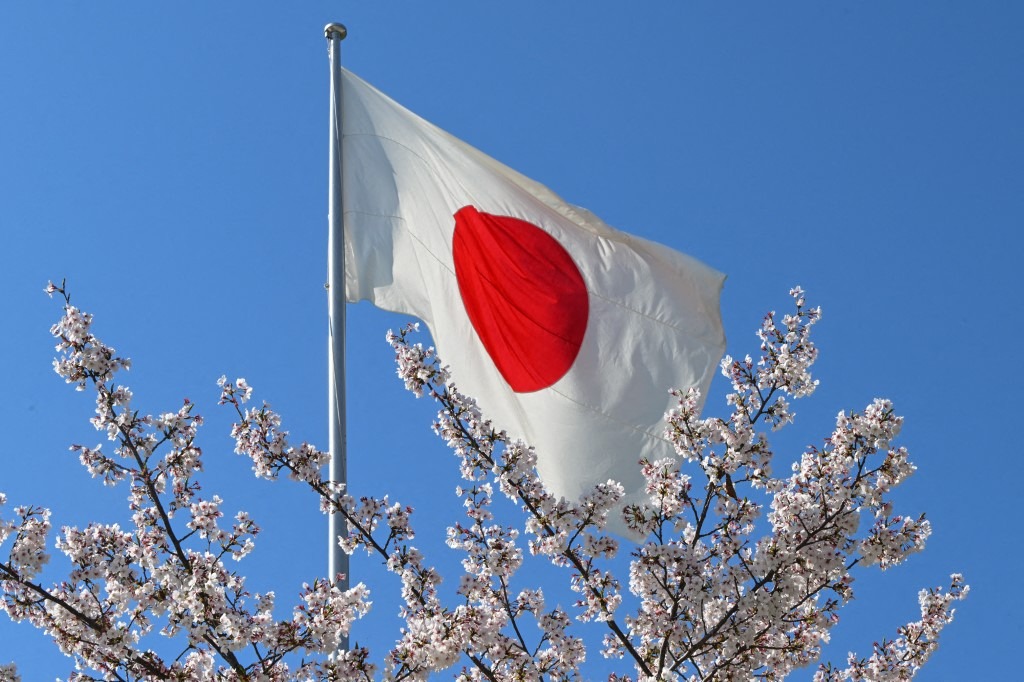 The Japanese national flag waves amidst blooming cherry blossoms under a clear sky in Hiroshima, Japan, on April 5, 2026.
