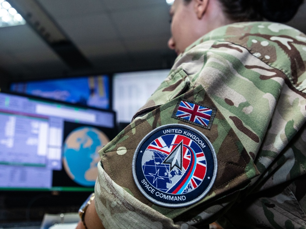 Close-up of a UK Space Command patch on a military uniform inside a satellite operations center.