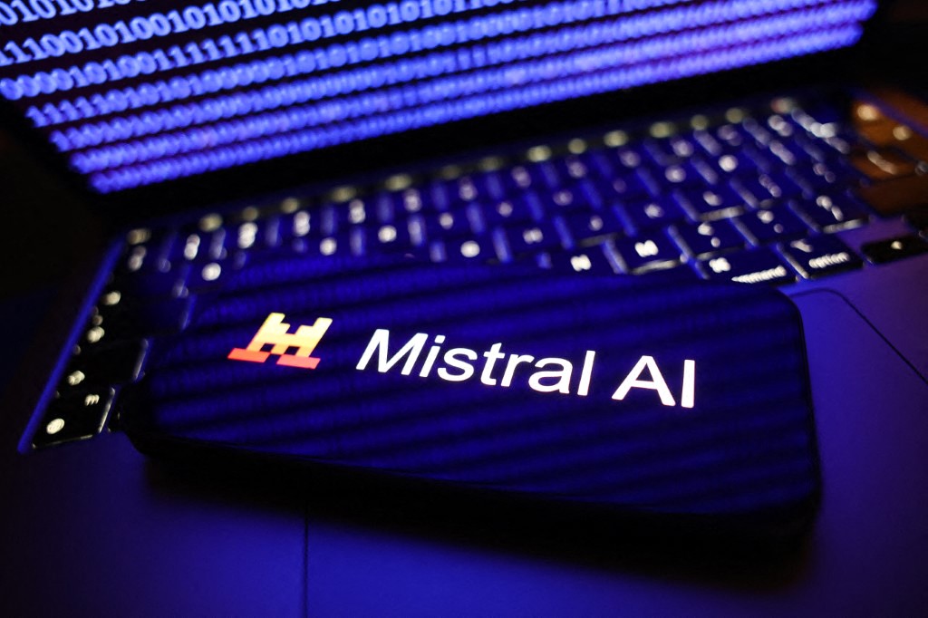 A binary code displayed on a laptop screen and Mistral AI logo displayed on a phone screen are seen in this illustration photo.