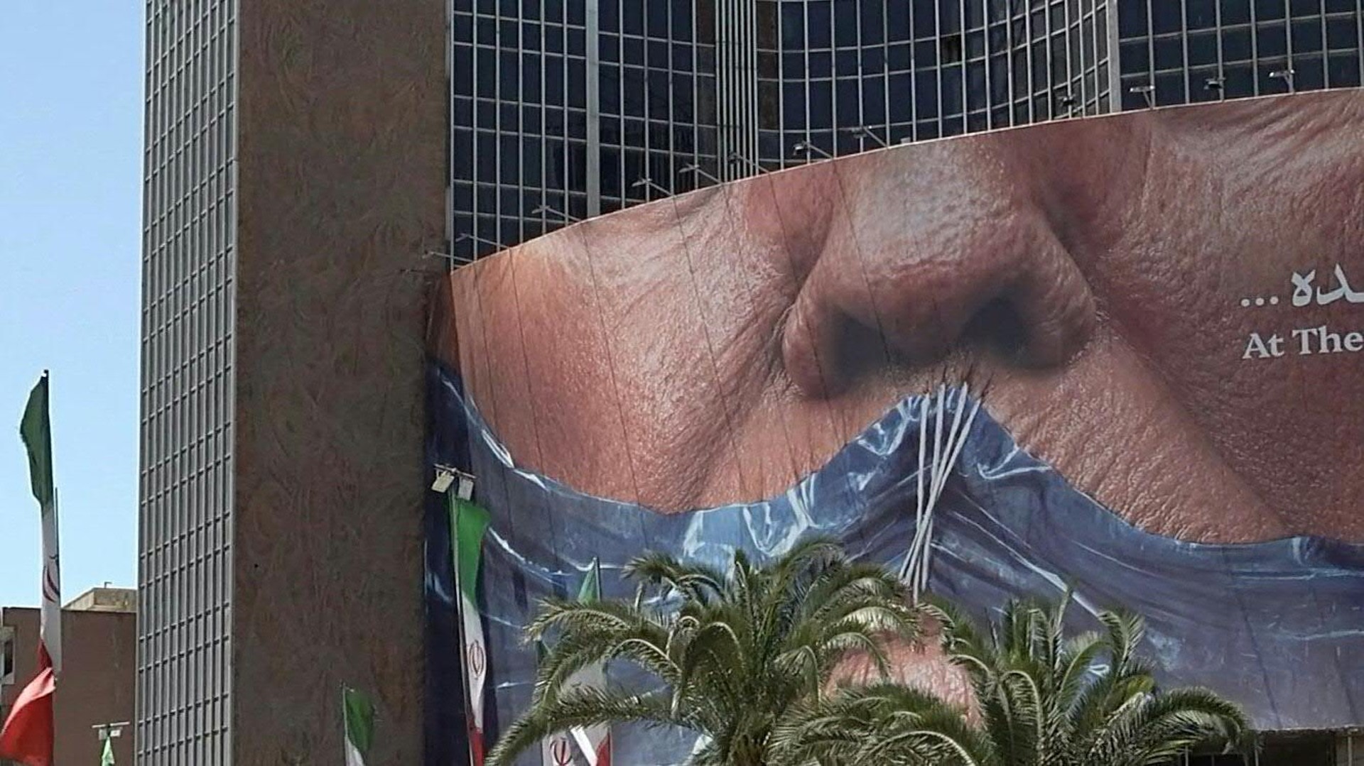 Daily life in Tehran during Eid al-Adha, with shoppers, traffic and Iranian flags seen near a large anti-US billboard showing US President Donald Trump, the Strait of Hormuz and the words 